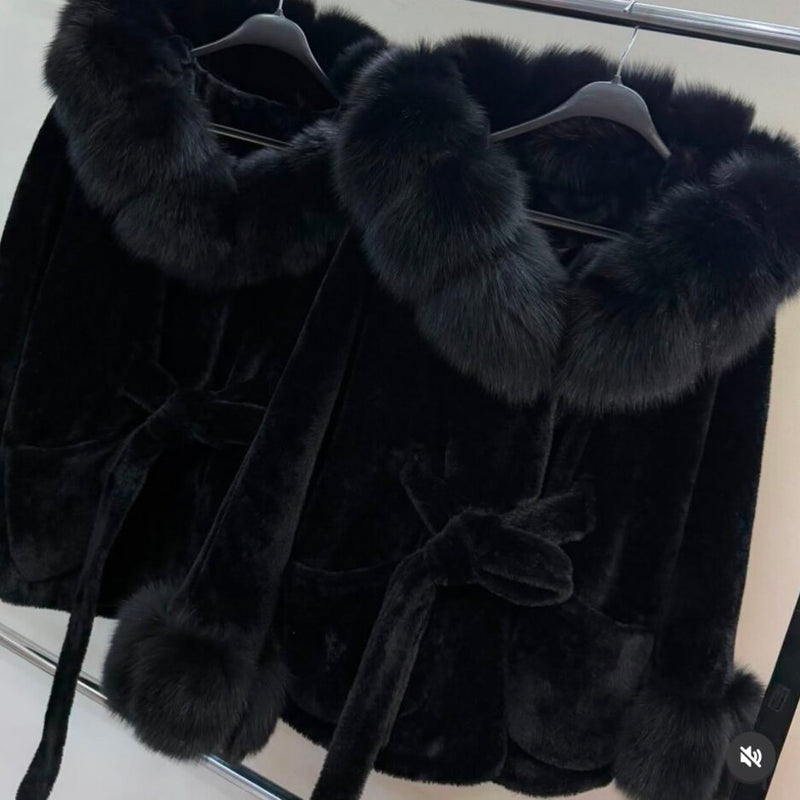 Black fur coat with fox trim hanging on a rack.