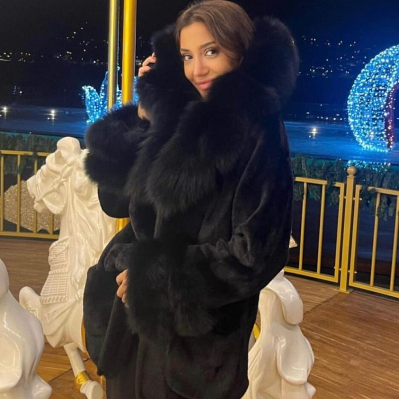 Woman in a black fur coat taking a selfie at night with decorative lights in the background.