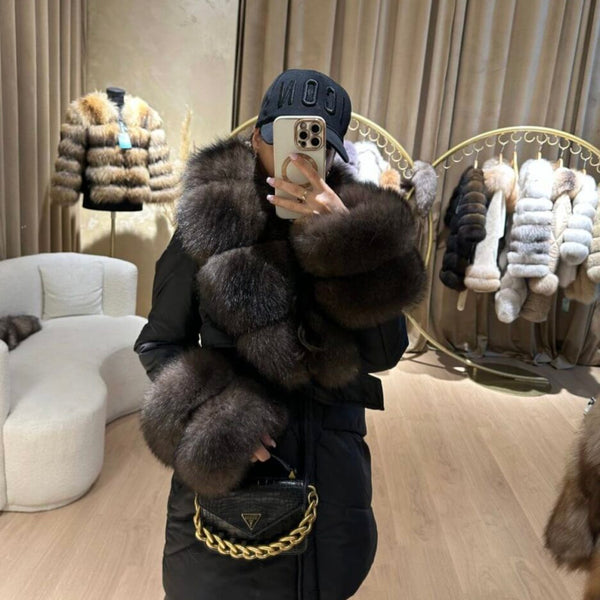 Person wearing a fur vest and taking a mirror selfie in a store with fur coats displayed.