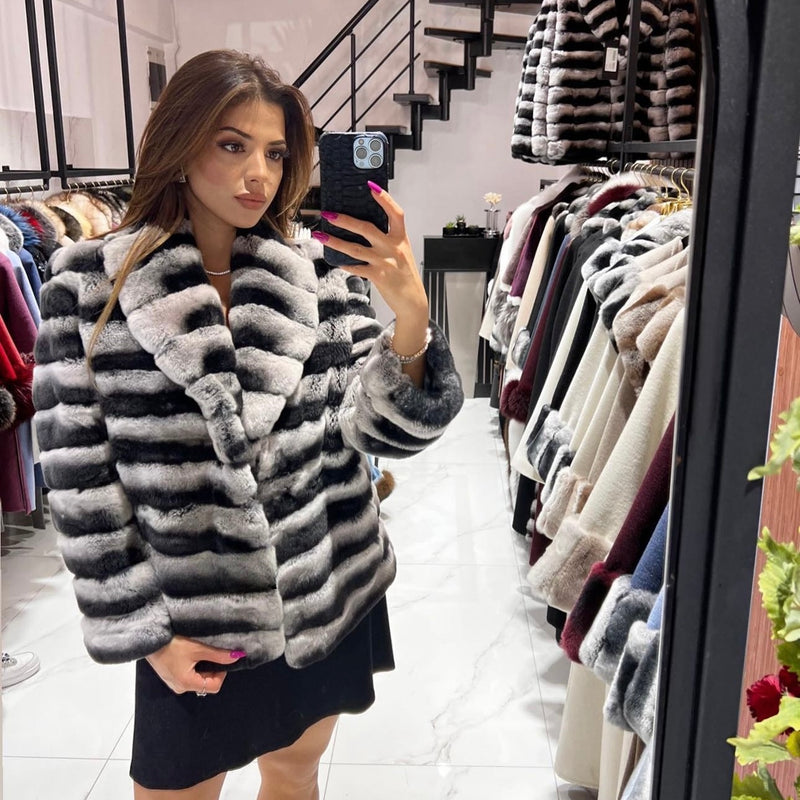 Woman taking a mirror selfie wearing a striped fur coat in a clothing store.