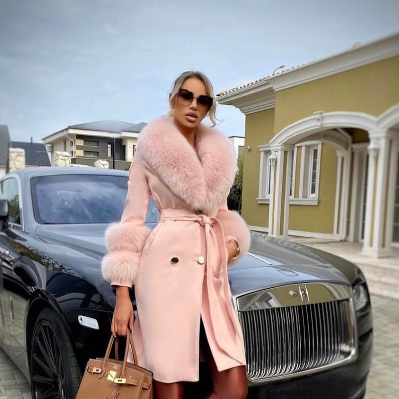 Woman in a pink coat standing next to a black luxury car with a house in the background