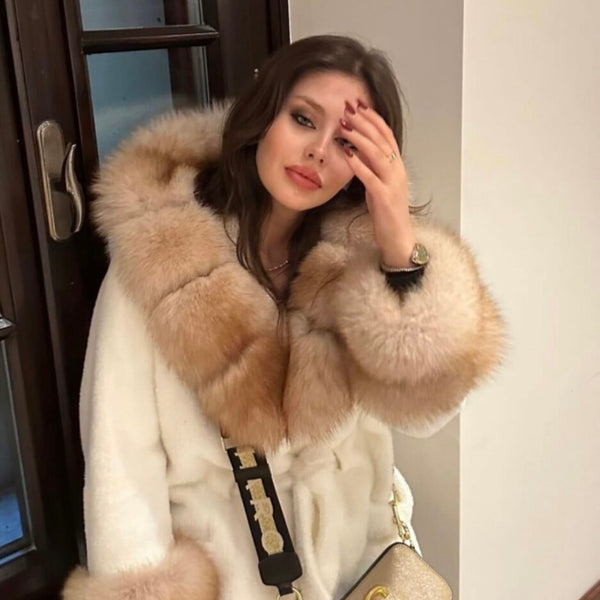Woman wearing a fur-trimmed coat with a handbag indoors.