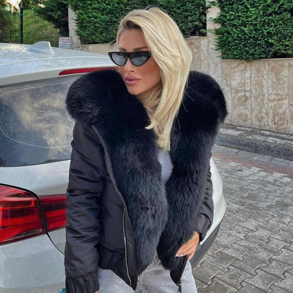 Woman in a black fur-lined coat standing next to a car on a sidewalk.