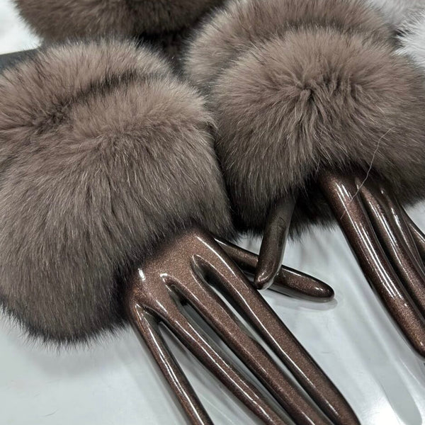 Pair of brown fur mittens with metallic handles on a reflective surface
