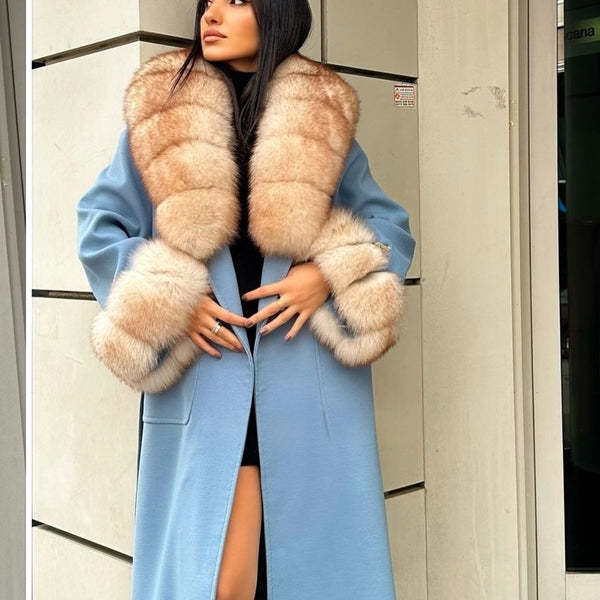 Woman wearing a long light blue coat with a fur collar in an indoor setting.