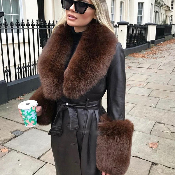 Woman wearing a dark coat with fur trim on a city street.