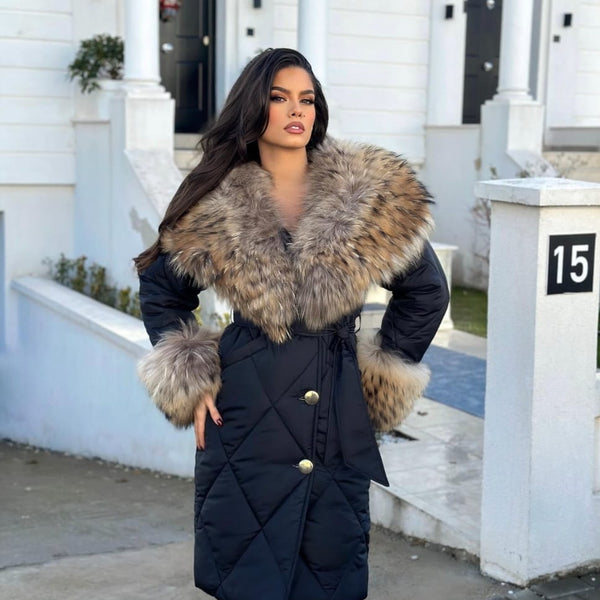 Woman wearing a black coat with fur trim standing in front of a white house.
