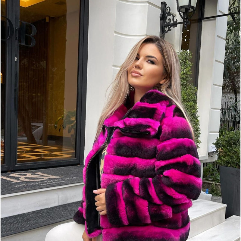 Woman wearing a bright pink and black fur coat standing outside a building.
