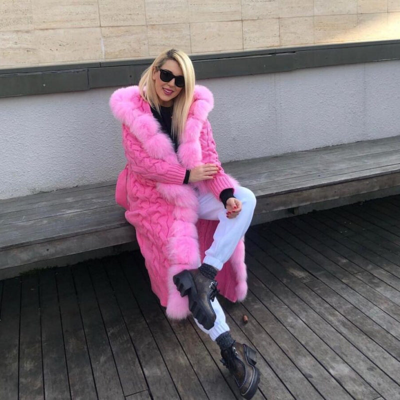 Woman wearing a pink fur coat sitting on a bench.
