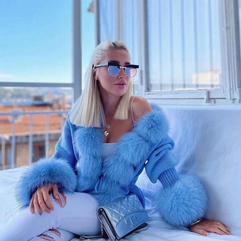 Woman wearing a blue fur coat and sunglasses indoors.